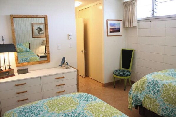 Un dormitorio con dos camas, un aparador, una silla, un espejo y una puerta que da a otra habitación.