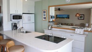 A modern kitchen with white cabinetry, a built-in microwave, a stove, and a large island with bar stools.