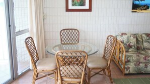A dining area with wicker chairs and a glass table, a sofa with a floral pattern, and a framed picture on the wall.