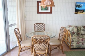 Un comedor con sillas de mimbre y una mesa de vidrio, un sofá con estampado floral y un cuadro en la pared.