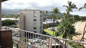 A balcony with a view of a building, palm trees, and a beach.