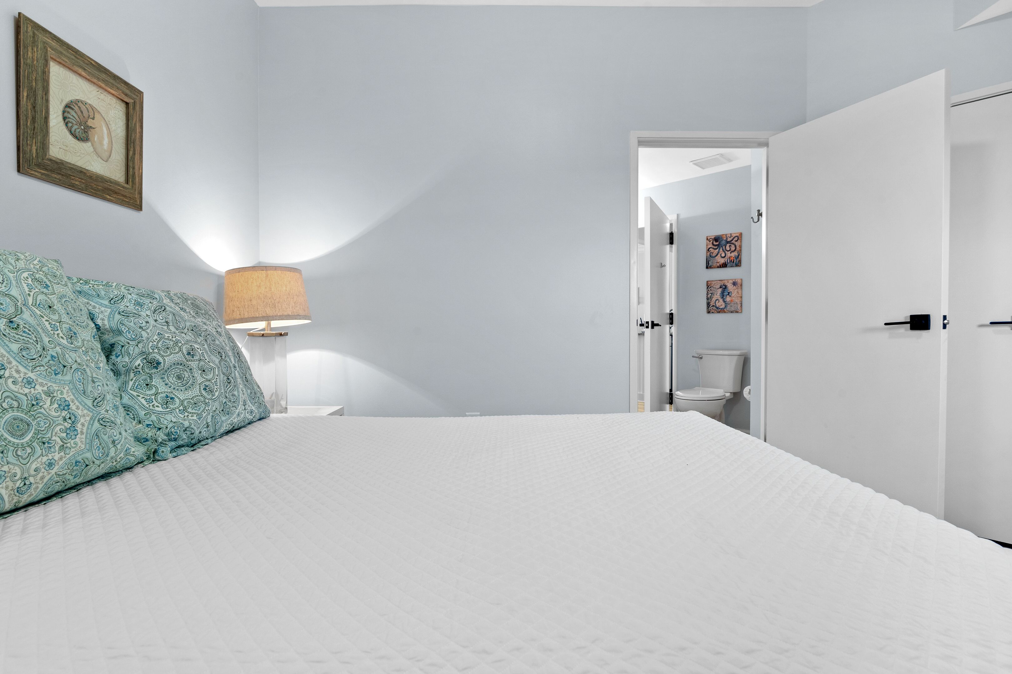 A bedroom with a bed, a bedside lamp, and a door leading to a bathroom.