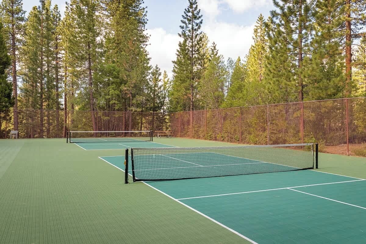 A tennis court with a net, surrounded by a fence and trees.