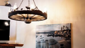 A chandelier with a rustic design, a painting of a lake landscape, and a flat-screen TV mounted on the wall. - Updated Interior, 2 Private Decks, Gas Fireplace and Community Pool in Summer! (Kings Beach)