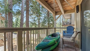 A covered porch with a green kayak, a blue chair, and a view of tall trees. - Updated Interior, 2 Private Decks, Gas Fireplace and Community Pool in Summer! (Kings Beach)