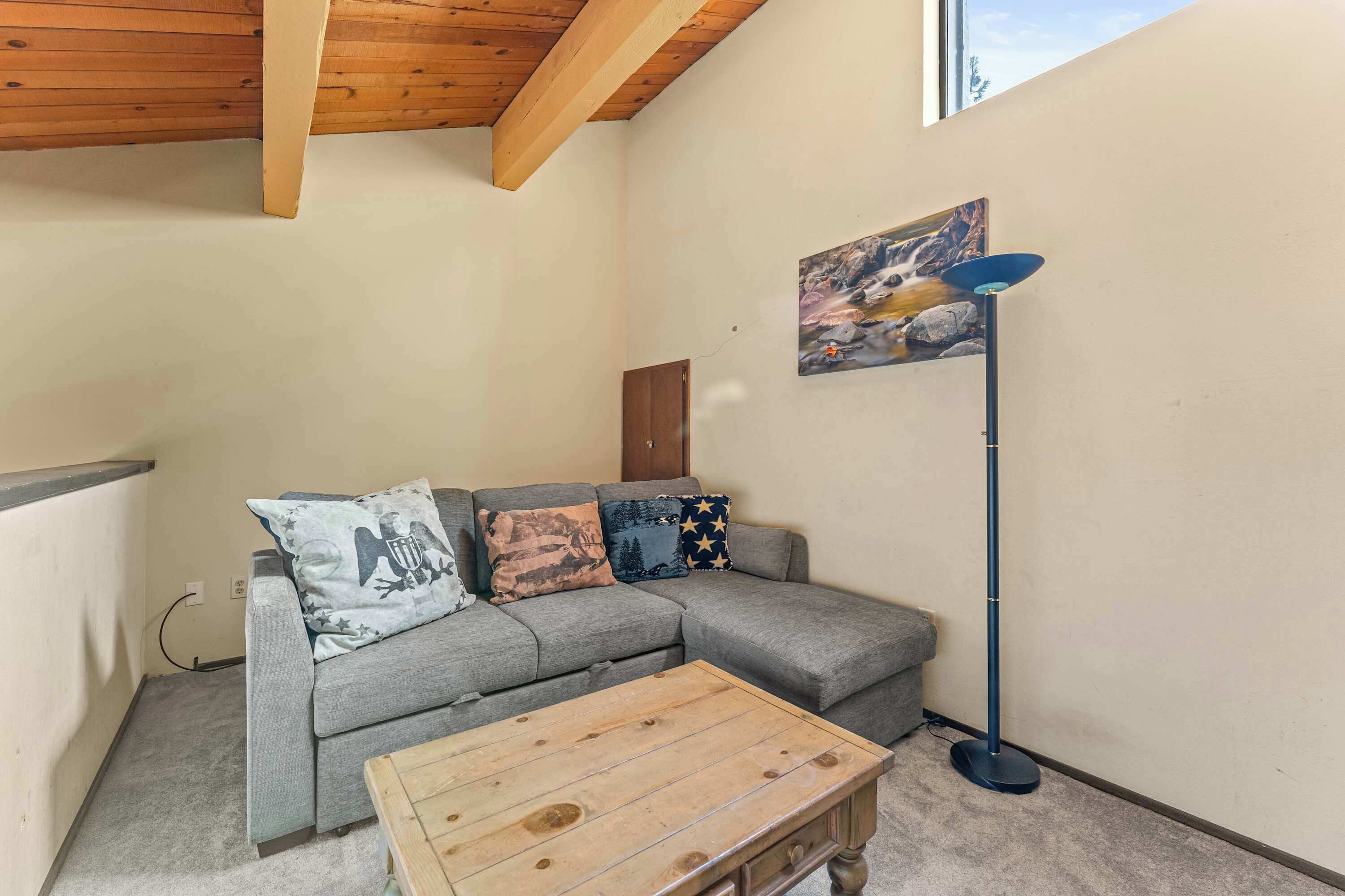 A living room with a grey sectional sofa, a wooden coffee table, a floor lamp, and a painting on the wall.