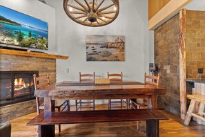 A dining area with a rustic wooden table, chairs, a fireplace, and a painting of a landscape.