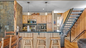 A kitchen with a central island, wooden bar stools, a staircase, and a stone accent wall. - Updated Interior, 2 Private Decks, Gas Fireplace and Community Pool in Summer! (Kings Beach)