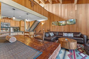 A spacious living area with a wooden floor, a brown leather sofa, a coffee table, and a dining table.