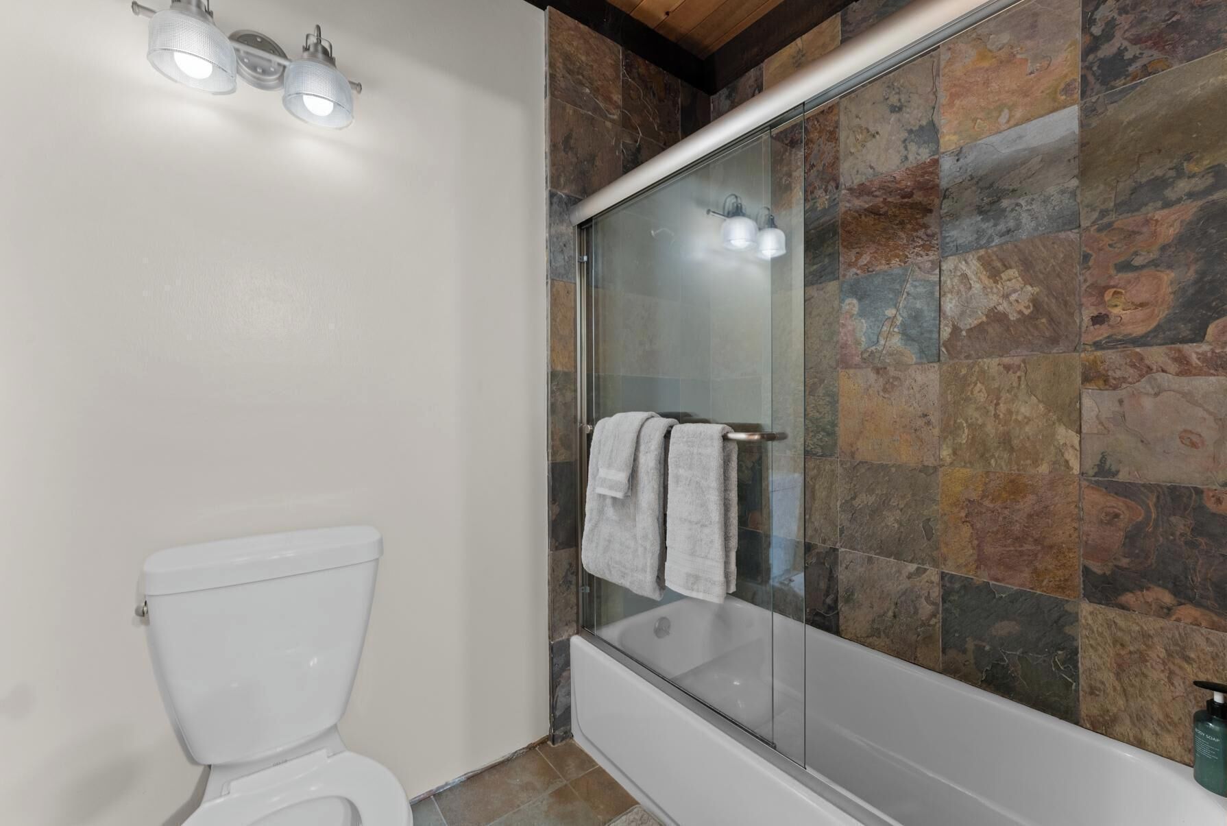 Un baño con inodoro, ducha envuelta en vidrio con puerta de cristal y bañera.