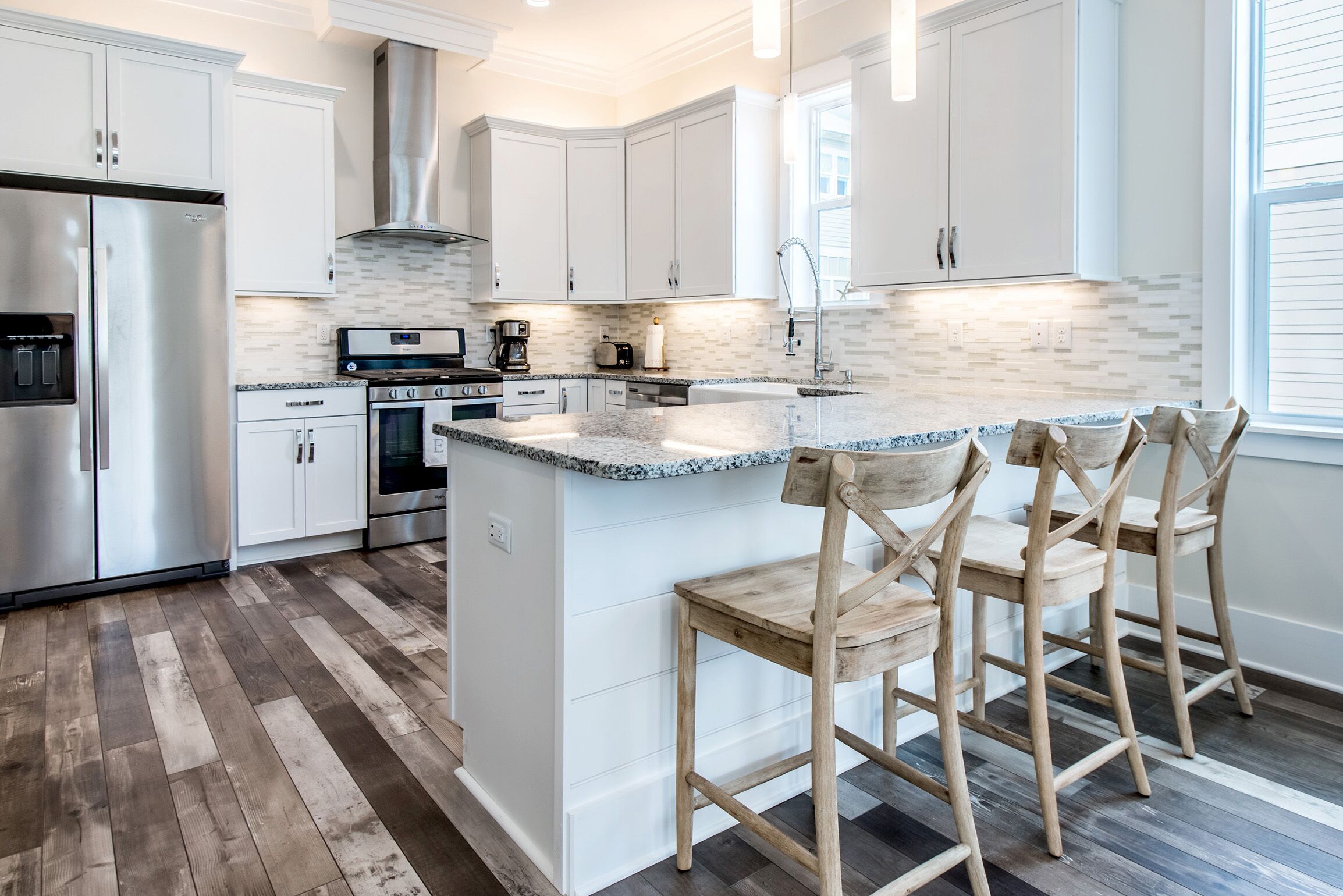 A modern kitchen with white cabinetry, a stainless steel refrigerator, a built-in oven, and a granite countertop island with bar stools.