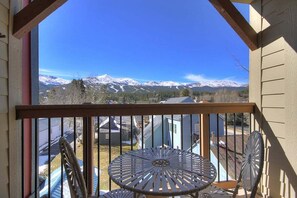 Un balcon offrant une vue sur des montagnes enneigées, une table en métal et deux chaises.