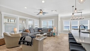 A spacious living area with a grey sofa, a coffee table, and a dining area with a kitchen island and bar stools. - Las Olas - Oceanfront Vacation Home with Private Pool Space & Gulf Views (Miramar Beach)