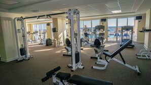 Un gimnasio con diversos equipos de ejercicio, amplias ventanas y vista al océano.