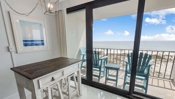 Una habitación con una mesa y sillas de madera, un cuadro en la pared y vista a la playa a través de puertas de vidrio grandes.