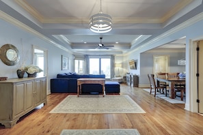 A spacious living room with a blue sofa, wooden dining table, and a ceiling fan. - Beautiful Oceanfront Turtle Lane Villa in Sea Pines with Multiple Pools! (Hilton Head Island)