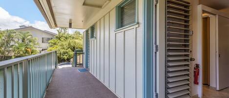 A covered outdoor corridor with a metal door, a fire extinguisher, and a view of a residential area with palm trees.