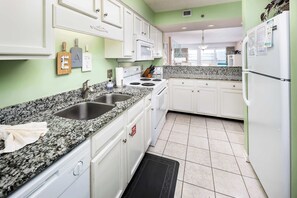 A kitchen with white cabinets, a granite countertop, a stainless steel sink, a stove, and a refrigerator.