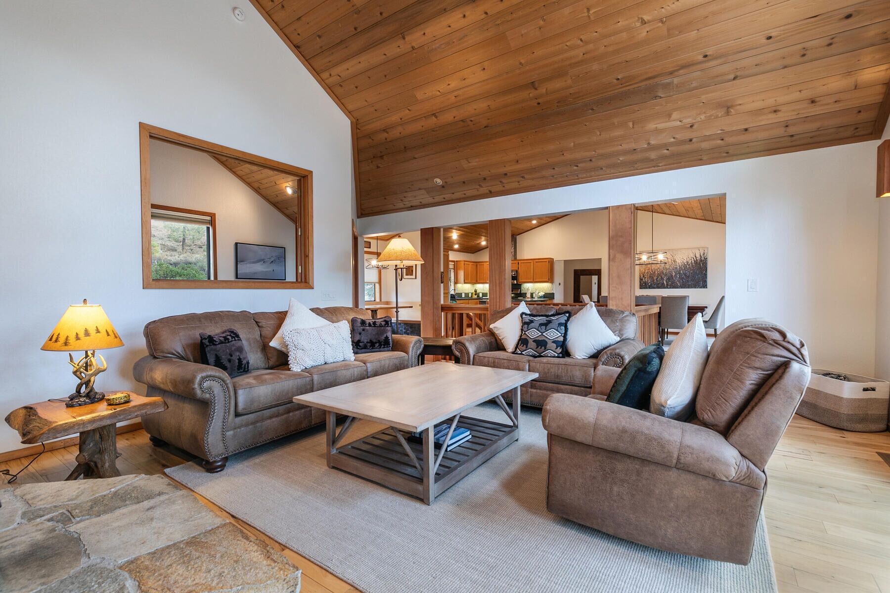 A spacious living room with a wooden ceiling, leather sofas, a coffee table, and a stone accent wall.