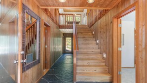 A wooden interior with a staircase leading to a second floor, stone flooring, and wooden doors.
