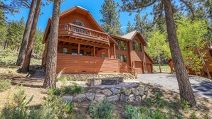 A wooden cabin with a balcony, surrounded by trees and a stone foundation.