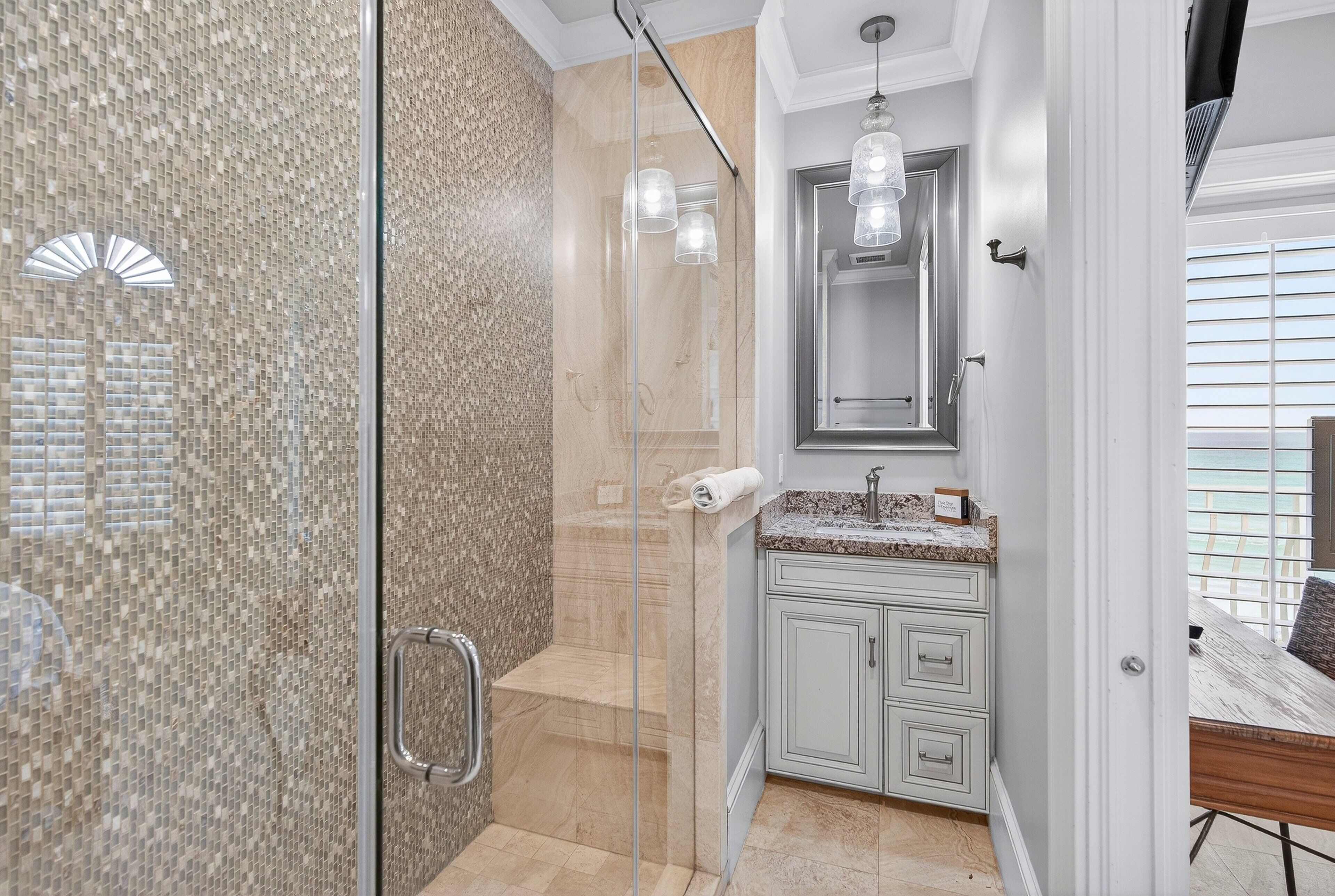 Een moderne badkamer met een douchecabine van glas, een wand betegeld met marmer, een wastafel met een granieten aanrechtblad, en een spiegel boven de wastafel.