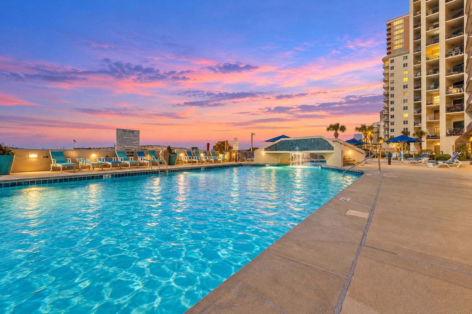 A swimming pool with lounge chairs and a hotel building in the background.