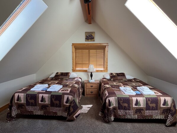 Une chambre confortable située sous les toits, avec deux lits, une table de chevet, une lampe et une fenêtre avec des stores.