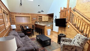 A cozy living room with a brown sofa, a patterned armchair, a coffee table, and a TV mounted on the wall. - Roomy Taylor Canyon Cabin With Private Fishing Access (Almont)