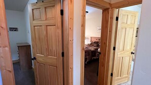 A hallway with wooden doors leading to a bedroom with a bed and a headboard. - Roomy Taylor Canyon Cabin With Private Fishing Access (Almont)