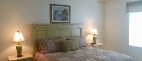 A bedroom with a bed, two bedside tables, a ceiling fan, a painting, and a window with curtains.