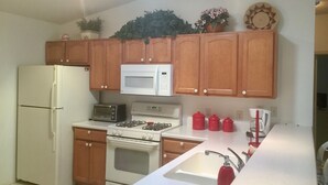 A kitchen with wooden cabinets, a white refrigerator, a microwave, a stove, a sink, and red kettles.
