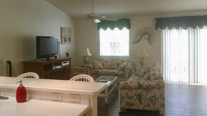 A living room with a television, two sofas, a dining table, and a ceiling fan.