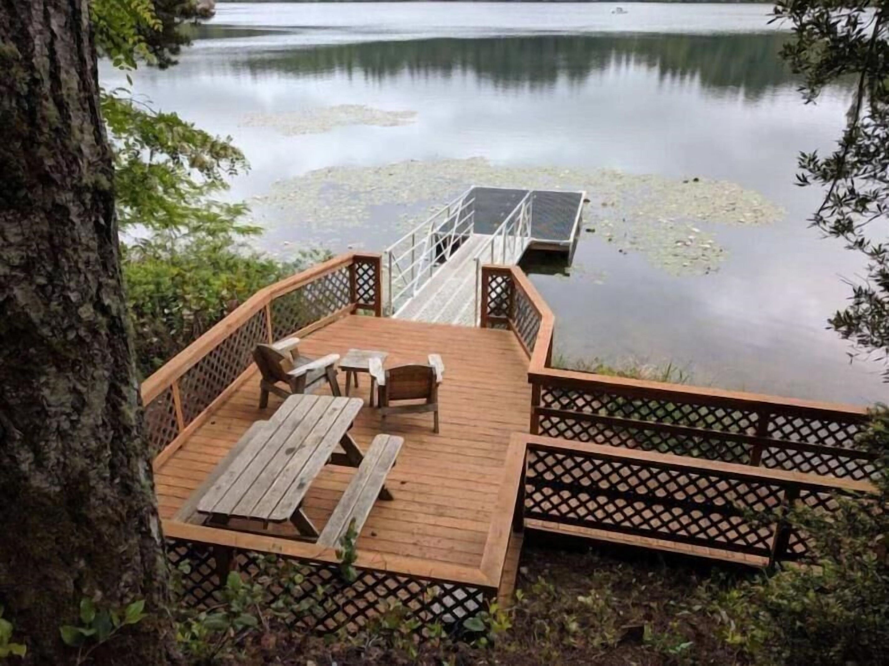 Une terrasse en bois avec une table et des chaises, donnant sur un lac paisible parsemé de nénuphars.
