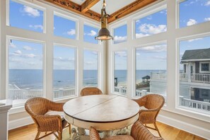 A round table with wicker chairs in a room with large windows overlooking the ocean. - Oceanfront 8BR Corolla retreat with pool, hot tub, and beach access. (Corolla)