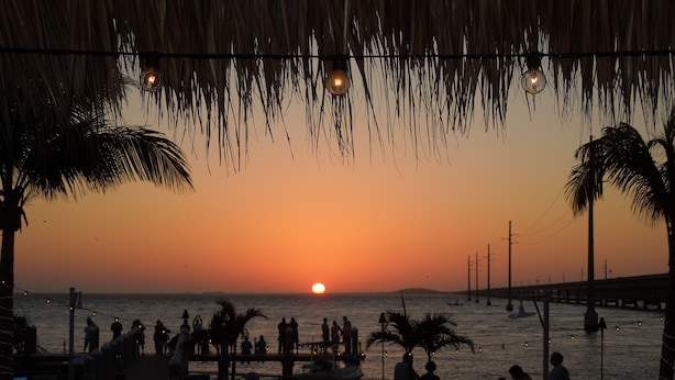 A sunset view from a beachside restaurant with outdoor seating and palm trees. - *Summer Special $2,775 Week* with a private chilled pool & 75' of dockage (Key Colony Beach)