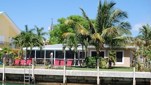 A waterfront property with a pool, red lounge chairs, and palm trees. - *Summer Special $2,775 Week* with a private chilled pool & 75' of dockage (Key Colony Beach)