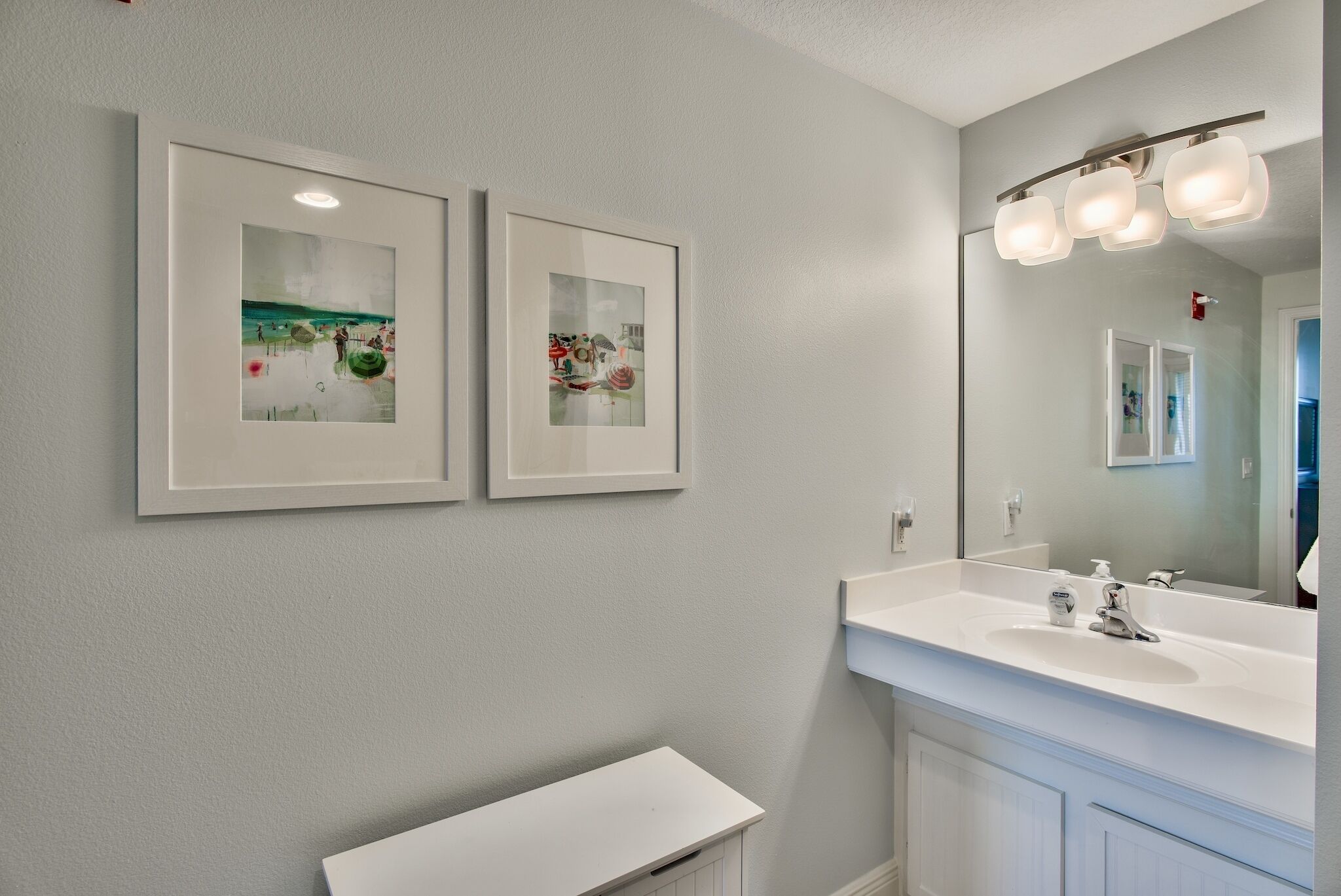 A bathroom with a white vanity, a large mirror with lights, and two framed pictures on the wall.