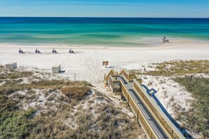 Ein Strand mit einem hölzernen Steg, der zum Ufer führt, feinem Sand und einem klaren, blauen Meer.