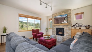 Una sala de estar con chimenea de piedra, ventanas amplias y un reposapiés rojo.