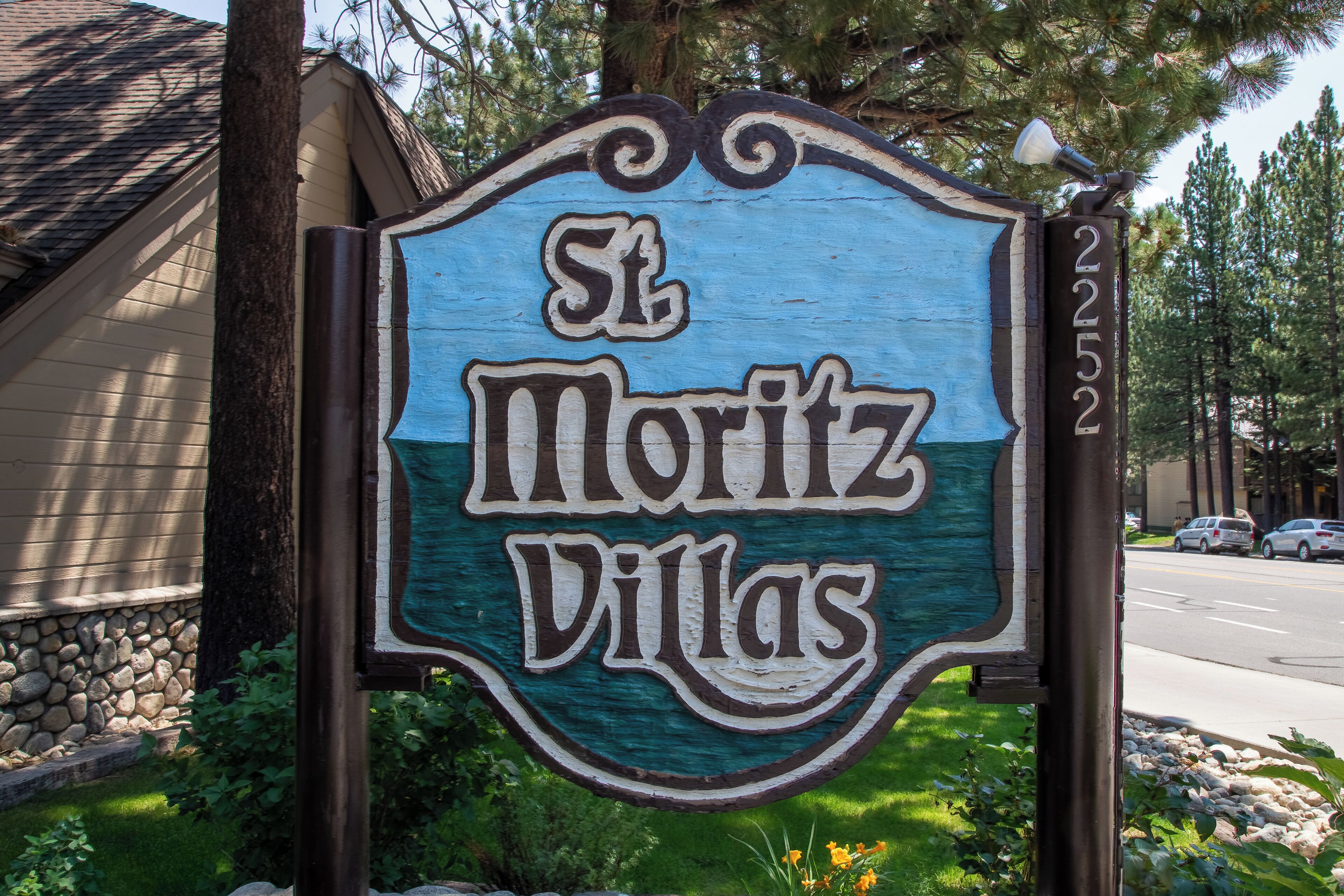 Een bord voor St. Moritz Villas met een rustiek ontwerp en een helder uitzicht op de omgeving, inclusief een weg en bomen.