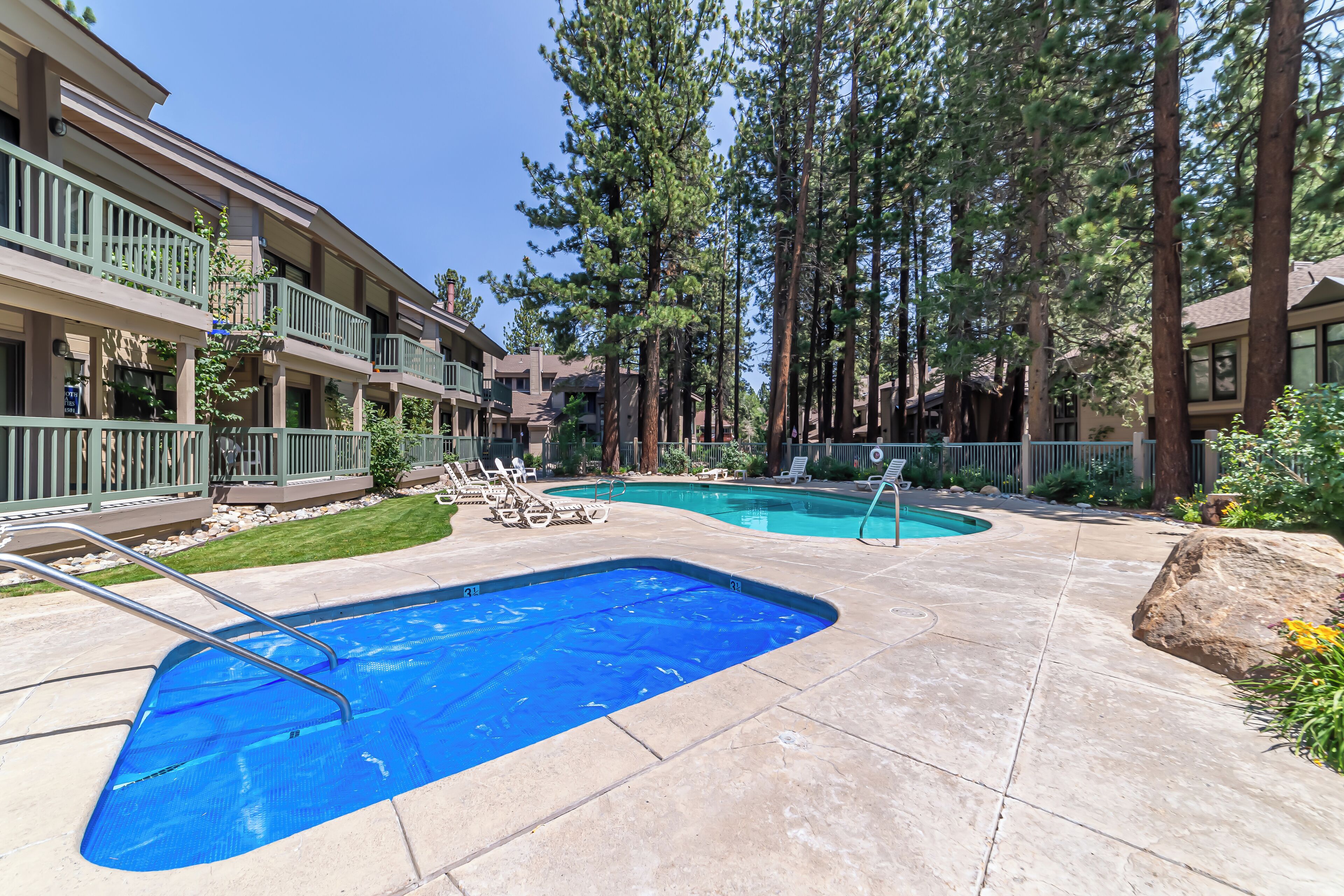 A pool area with two swimming pools, lounge chairs, and tall trees.
