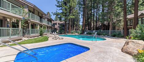 A pool area with two swimming pools, lounge chairs, and tall trees.