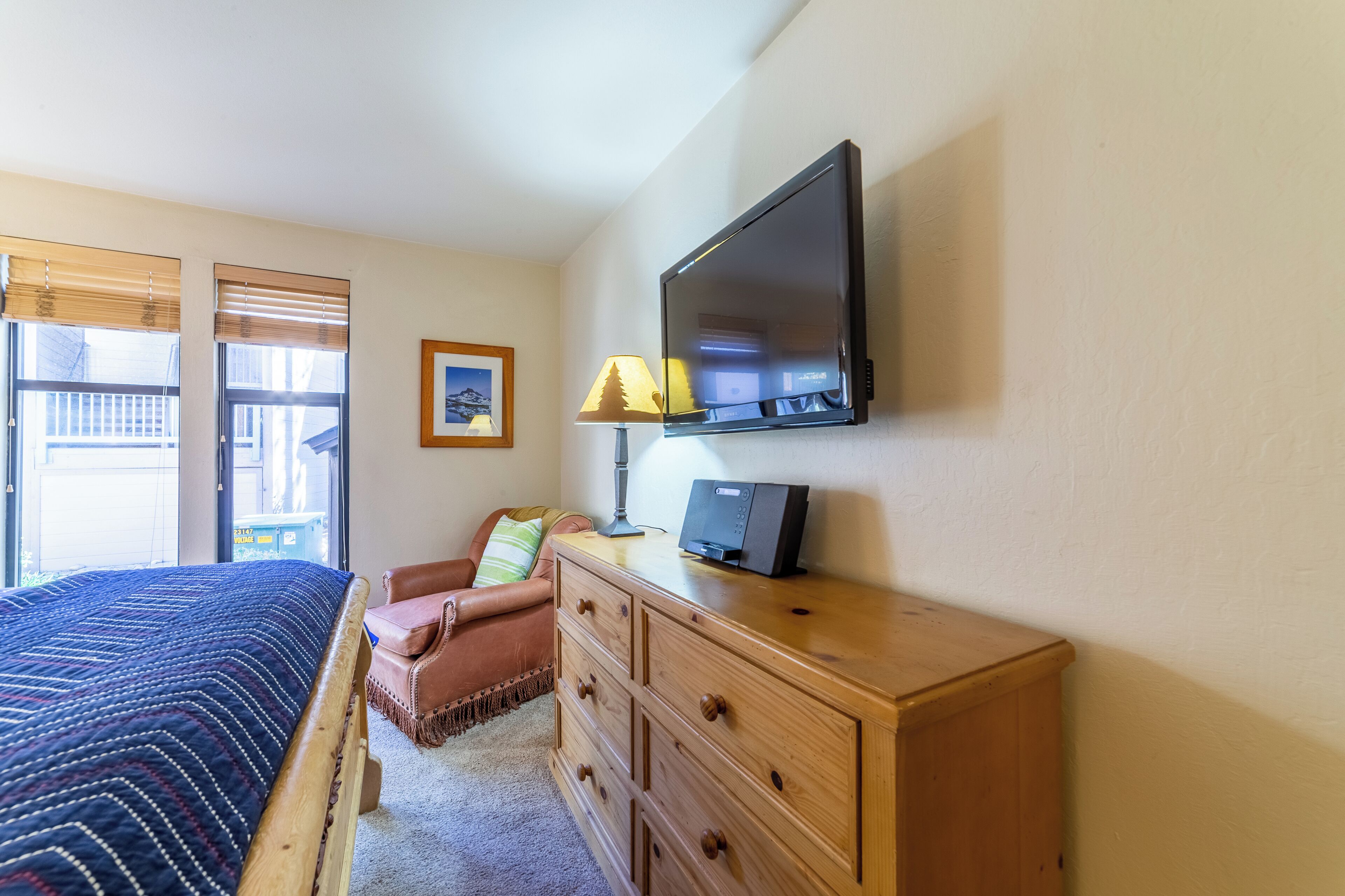 Un dormitorio con cama, cómoda, televisor, lámpara y ventana con persianas.