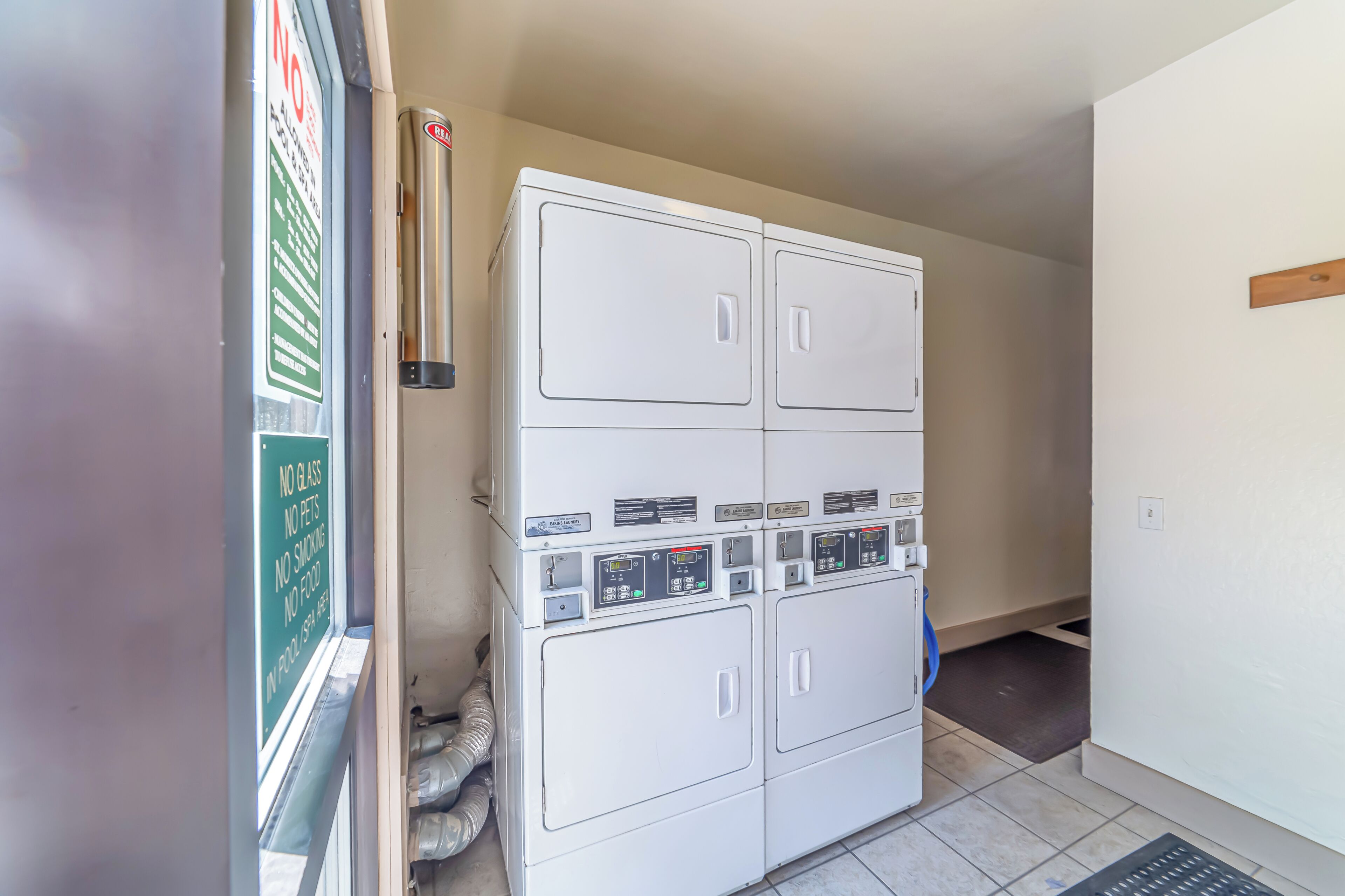 A laundry room with stacked washers and dryers, a vent, and a no glass sign.