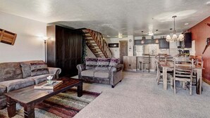A spacious living room with a sofa, a coffee table, and a staircase leading to a kitchen area. - Cimarron 301: Downtown Peak 9 Condo, Wood Fireplace, Pool & Sauna. (Breckenridge)