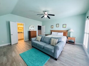 A bedroom with a bed, a ceiling fan, a nightstand, a dresser, a door to a bathroom, and a blue rug.