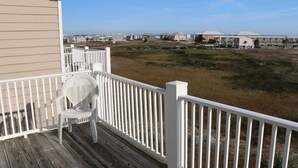 En träveranda med ett vitt räcke, en vit stol och en utsikt över hus och en strand i bakgrunden.