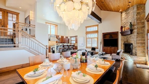 A spacious dining area with a long wooden table set for a meal, a chandelier, and a stone fireplace. - Luxury Home DV Mid Mountain, Skier Shuttle, Game/Theater Rooms, Hot tub (Deer Valley)