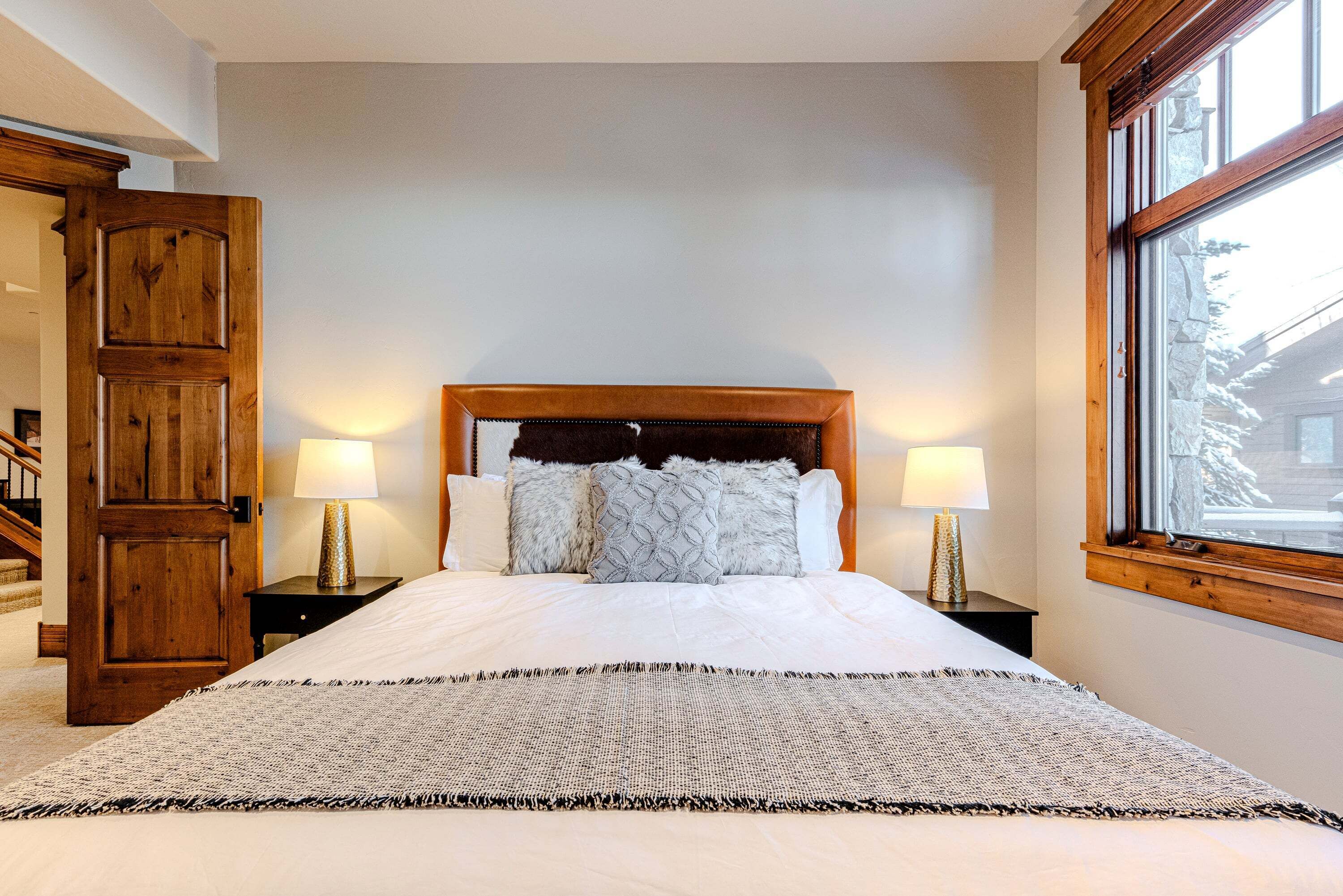 Un dormitorio con una cama grande, dos mesitas de noche con lámparas, un armario de madera y una ventana con vistas.